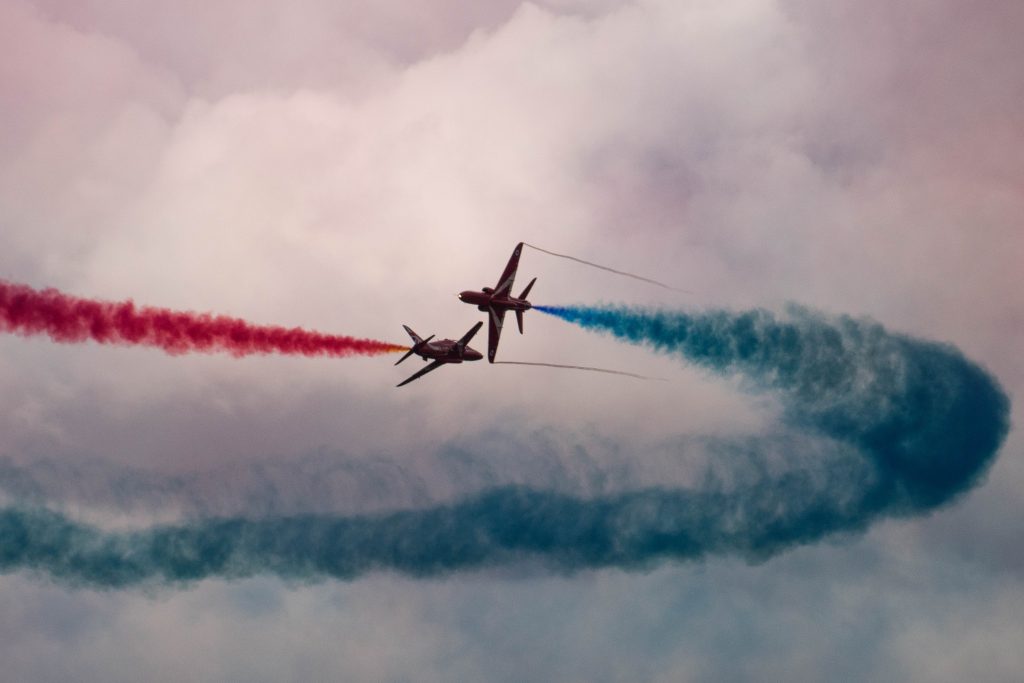 Two Red Arrows in flight, with red and blue smoke. 