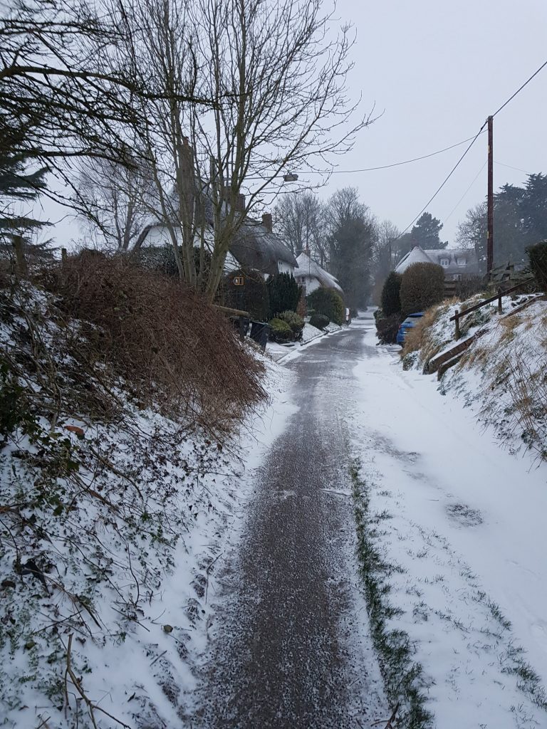 Wintry rural scene, a country lane with snow-covered thatched cottages.