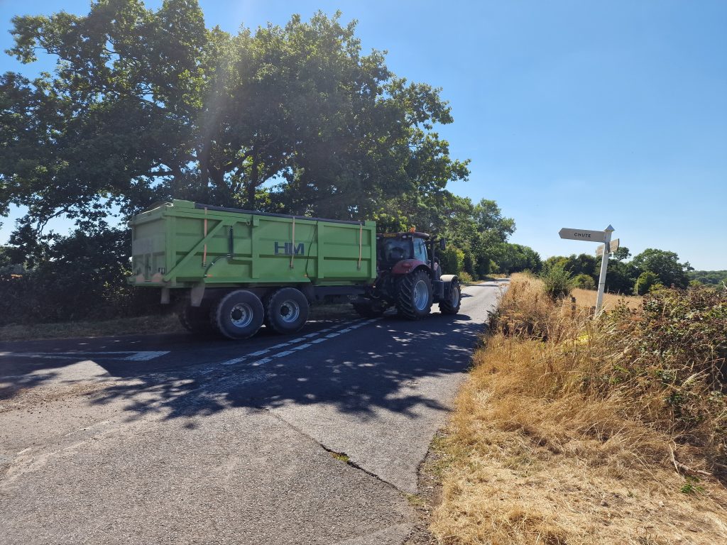 Bringing in the harvest - transporting the grain from the field. A red tractor and green trailer on a country lane in the height of summer.