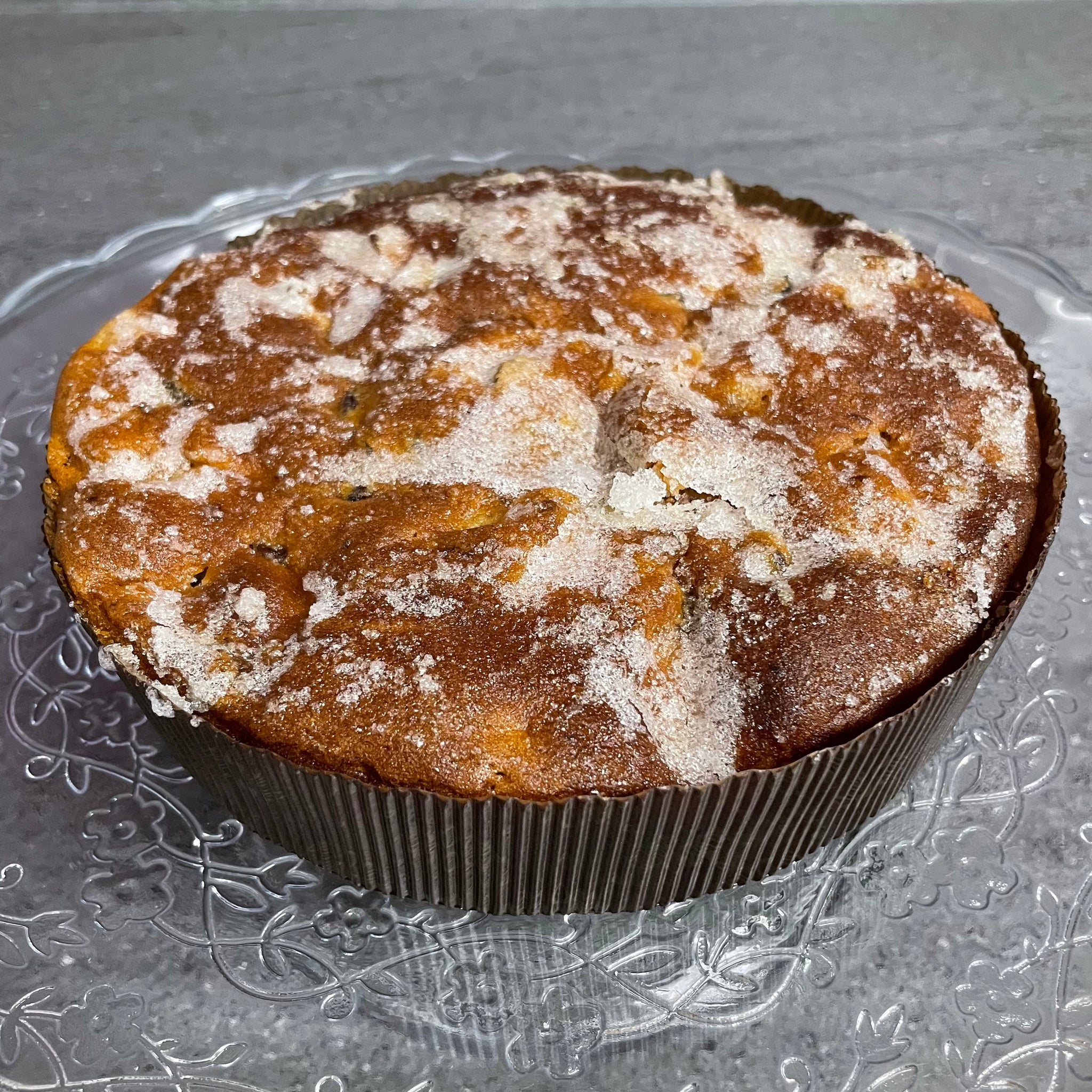 Homemade West Country apple and cider cake with a golden-brown top, dusted with a layer of sugar, displayed on a glass plate
